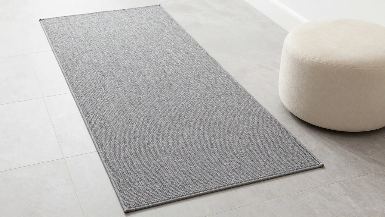Grauer Teppichläufer auf hellen Fliesen mit einem gemütlichen cremefarbenen Sitzpuff im Flur.